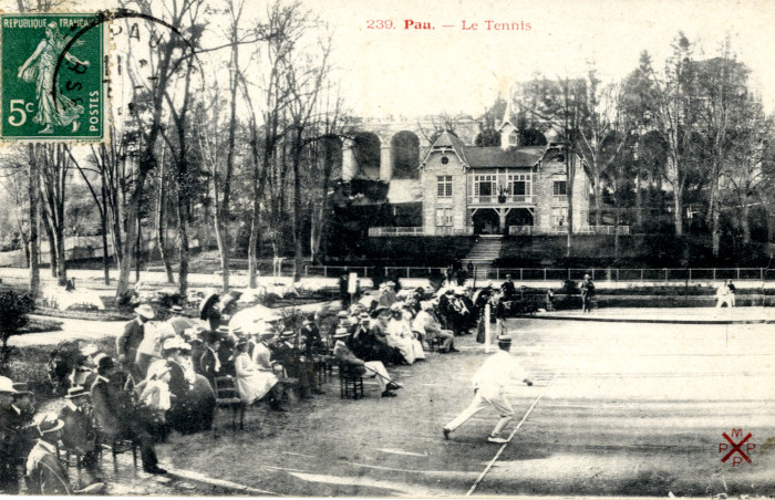 L’image représente un match de tennis au stade Tissié à Pau. A l'arrière-plan, le chalet du Véloce-club béarnais.